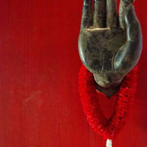 A hand of Buddha on a red door in Thailand with a red garland