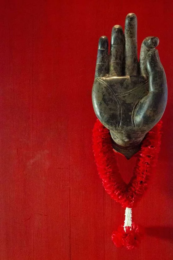 A hand of Buddha on a red door in Thailand with a red garland