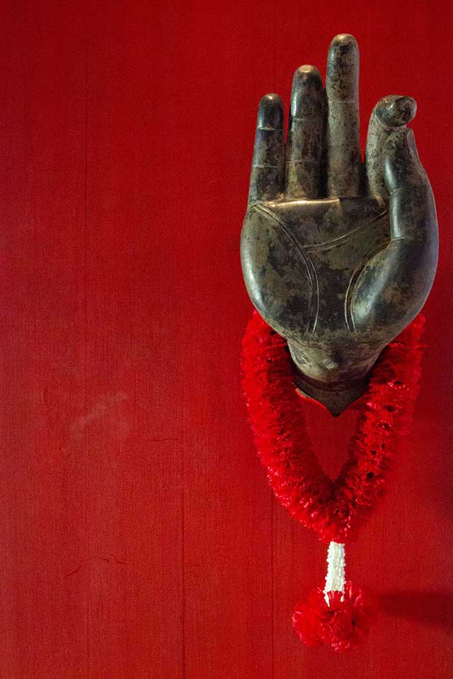 A hand of Buddha on a red door in Thailand with a red garland